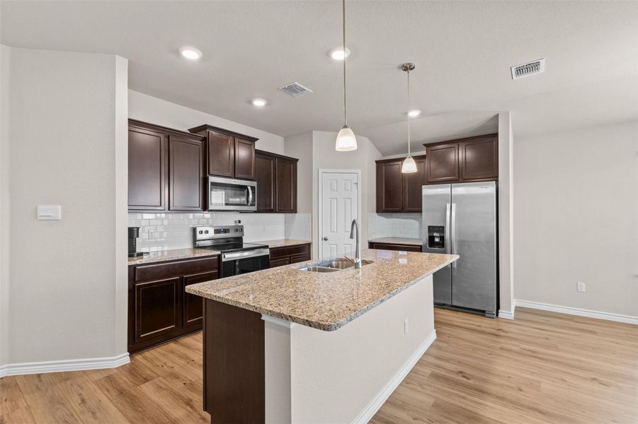 Kitchen with stainless steel appliances, dark wood finish cabinets, light stone countertops, light wood-style floors, and pendant lighting