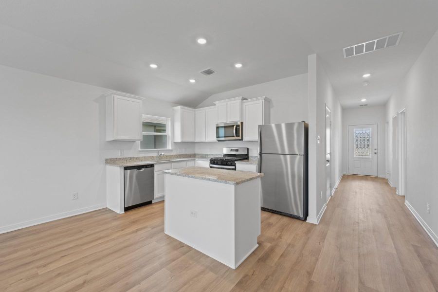 Kitchen with white cabinets, stainless steel appliances, a kitchen island, light wood finished floors, and recessed lighting