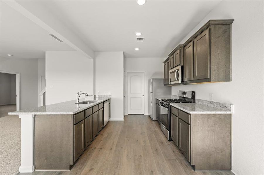 Kitchen featuring a peninsula, stainless steel appliances, light stone countertops, dark brown cabinetry, and recessed lighting Kitchen featuring a peninsula, stainless steel appliances, light stone countertops, dark brown cabinetry, and recessed lighting