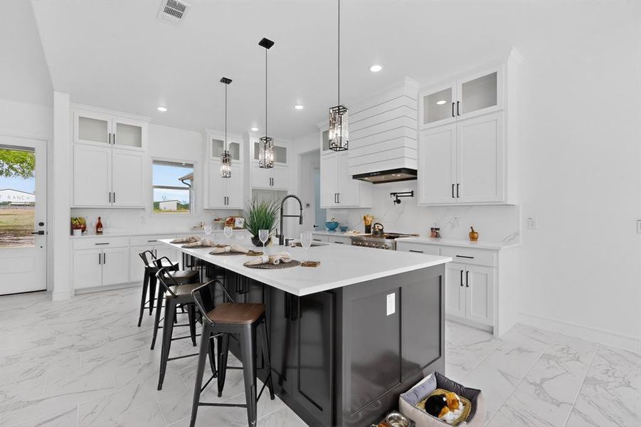 Spacious kitchen featuring a dark-toned island with seating, white shaker cabinetry, white countertops and backsplash, stainless steel appliances, and wood-finish tile flooring
