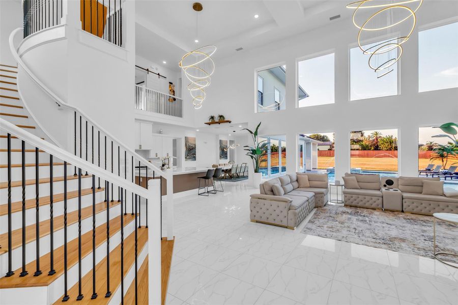 Great Room & Staircase:The sweeping staircase ascends as a sculptural centerpiece, grounding a space where soaring ceilings, oversized windows, and radiant chandeliers create a luminous backdrop. Here, gatherings unfold with ease and elegance, blending grandeur with effortless connection.