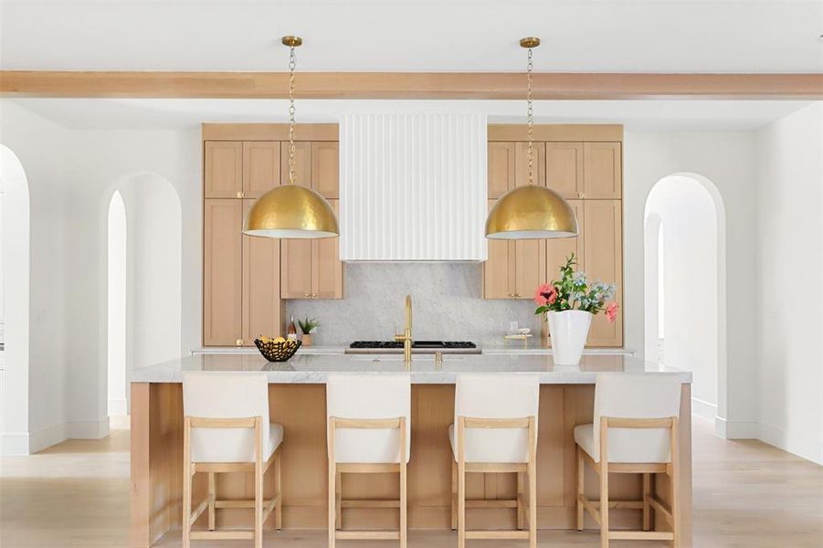 Kitchen featuring hanging light fixtures, an island with sink, backsplash, a breakfast bar, and light hardwood / wood-style floors