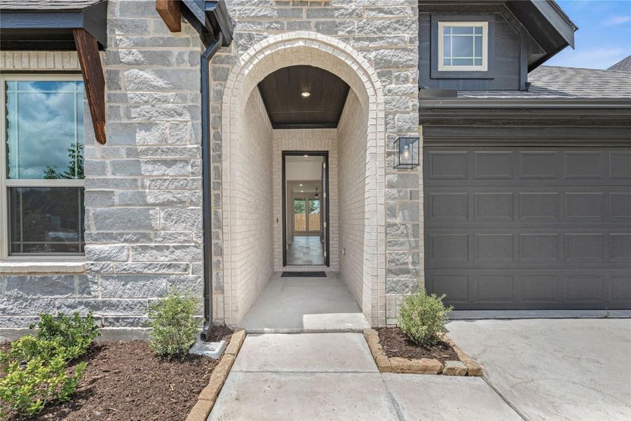 Home entrance with arched brick entryway, stone exterior, and two-car garage beside front door
