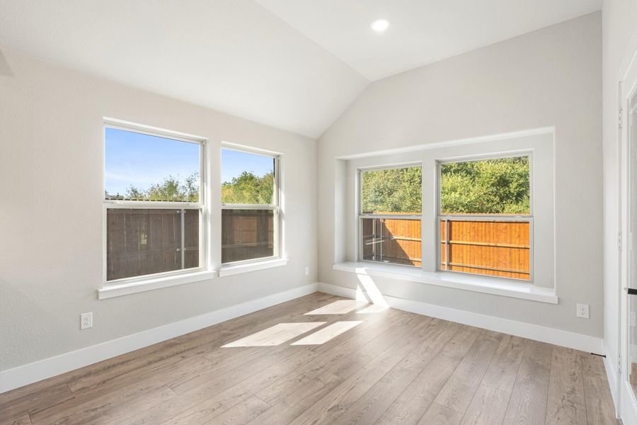 Empty bedroom with vaulted ceiling, hardwood floors, and a built-in window seat with backyard views