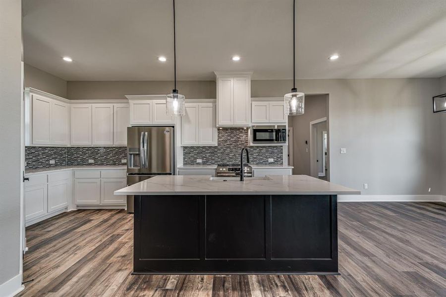 Kitchen featuring white cabinets, hanging light fixtures, a center island with sink, dark wood-type flooring, and stainless steel appliances