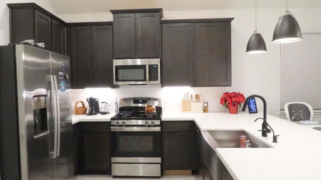 Modern kitchen featuring dark cabinetry and a farmhouse sink. The space is well-lit with pendant lights and under-cabinet lighting, creating a warm and inviting atmosphere. Modern kitchen featuring dark cabinetry and a farmhouse sink. The space is well-lit with pendant lights and under-cabinet lighting, creating a warm and inviting atmosphere.