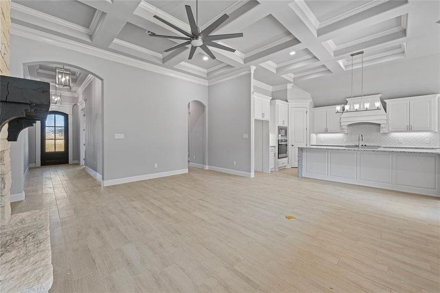 Unfurnished living room featuring light hardwood / wood-style flooring, crown molding, and ceiling fan with notable chandelier