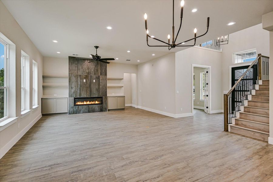 Unfurnished living room with a fireplace, a ceiling fan, light wood-type flooring, and a chandelier