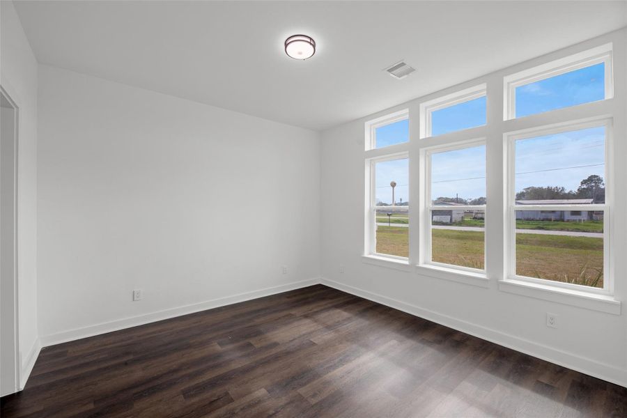 Airy room with large windows offering plenty of natural light and scenic views. Features sleek, dark wood flooring and a modern ceiling light. Perfect for a cozy family space or home office.