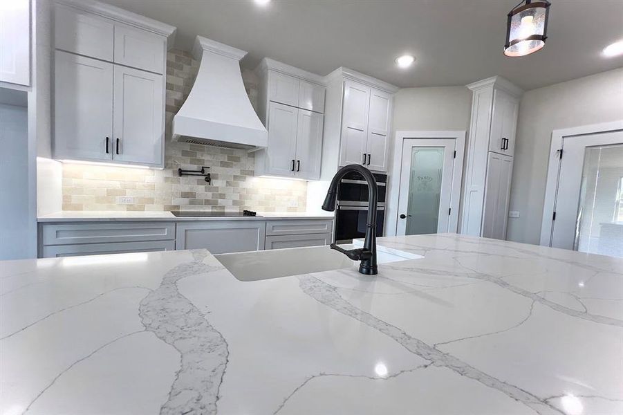 Kitchen featuring light stone counters, decorative backsplash, premium range hood, recessed lighting, and white cabinets