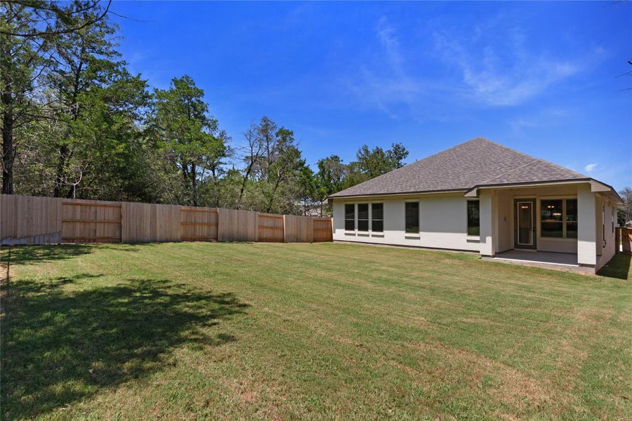 A well-maintained lawn stretches towards a newly constructed home, bordered by a privacy fence and natural tree line.