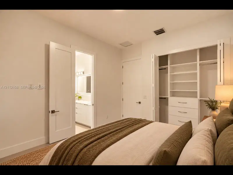 Comfortable bedroom with neutral walls, and a closet with built-in shelving and drawers