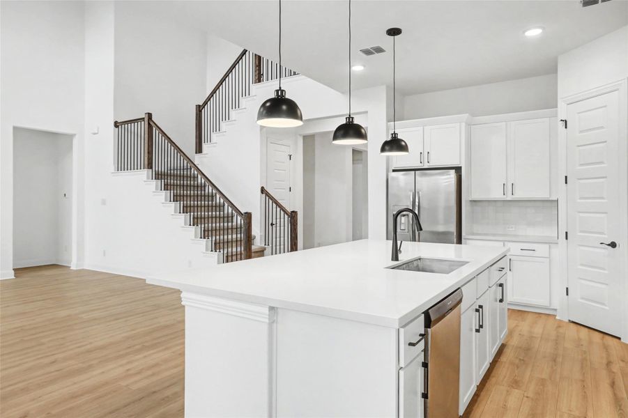 Kitchen with white cabinets, a center island with sink, light wood-style flooring, stainless steel appliances, and hanging light fixtures