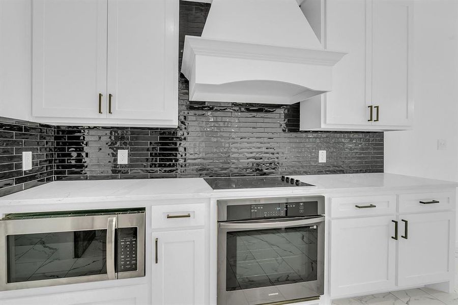 Kitchen with custom exhaust hood, white cabinetry, appliances with stainless steel finishes, and light tile patterned floors