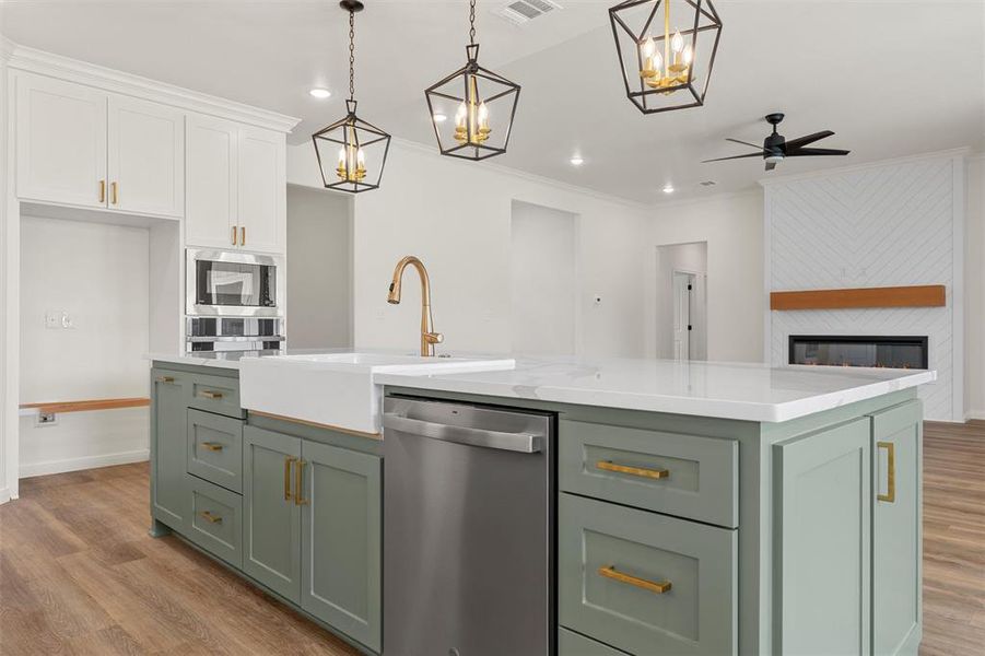 Kitchen featuring green cabinets, white cabinets, light wood-style flooring, appliances with stainless steel finishes, and ornamental molding Kitchen featuring green cabinets, white cabinets, light wood-style flooring, appliances with stainless steel finishes, and ornamental molding