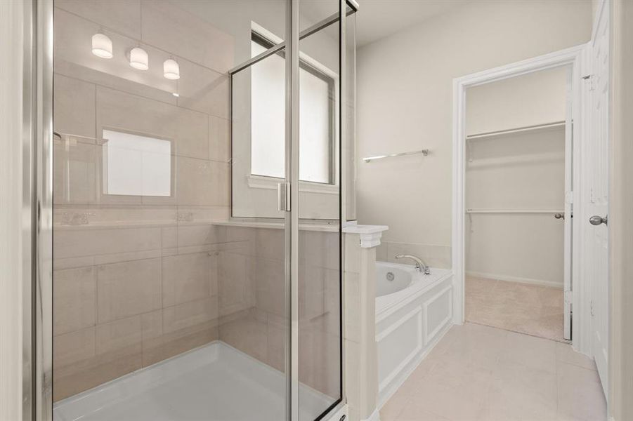 This additional view of your primary bathroom features tile flooring, fresh paint, walk-in shower, a separate garden tub, and a large walk-in closet.