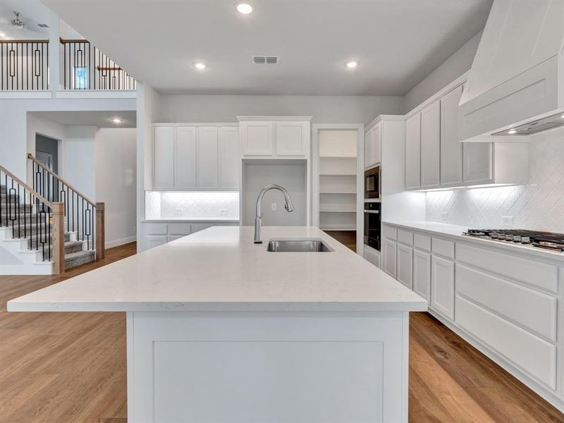 Kitchen with sink, stainless steel appliances, premium range hood, a kitchen island with sink, and light wood-type flooring