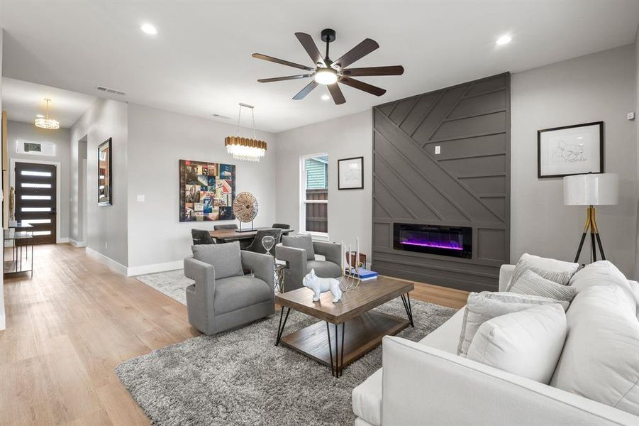 Living room with a large fireplace, ceiling fan, and light hardwood / wood-style flooring