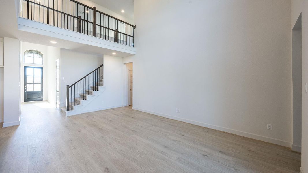 Unfurnished living room with light wood-style floors, a towering ceiling, stairs, and recessed lighting Unfurnished living room with light wood-style floors, a towering ceiling, stairs, and recessed lighting