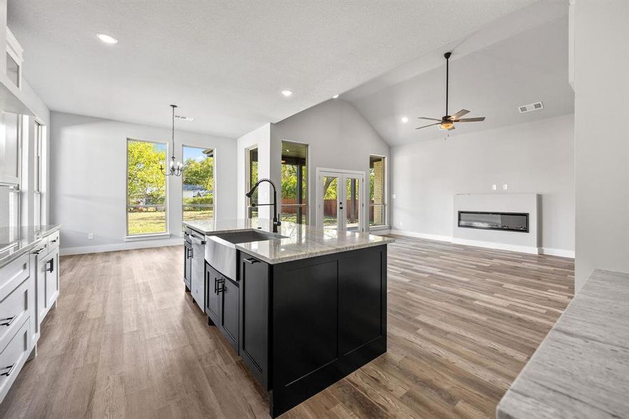 Kitchen with dark cabinetry, hanging light fixtures, a chandelier, light stone countertops, and a glass covered fireplace