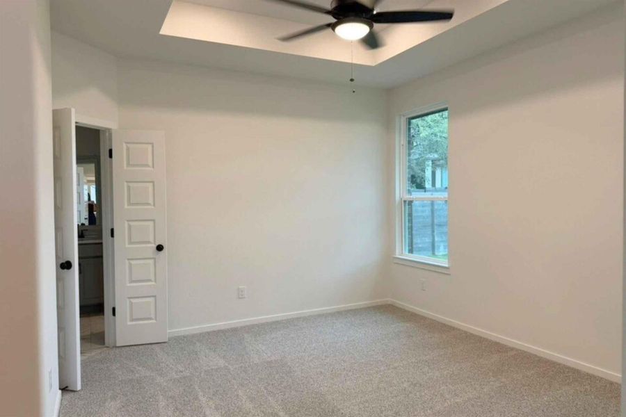 Spare room with a tray ceiling, light carpet, and a ceiling fan