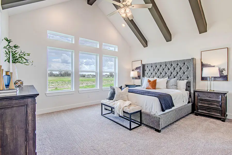 A striking retreat—this primary bedroom boasts vaulted ceilings with dark accent beams, plush carpeting, and abundant natural light through a trio of picture windows. A striking retreat—this primary bedroom boasts vaulted ceilings with dark accent beams, plush carpeting, and abundant natural light through a trio of picture windows.