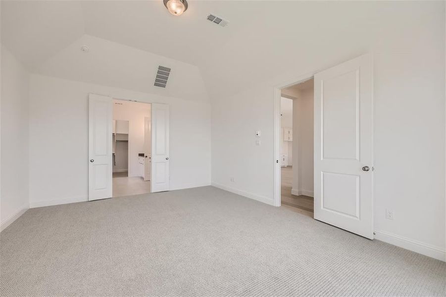 Unfurnished bedroom featuring carpet, a closet, a walk in closet, and lofted ceiling