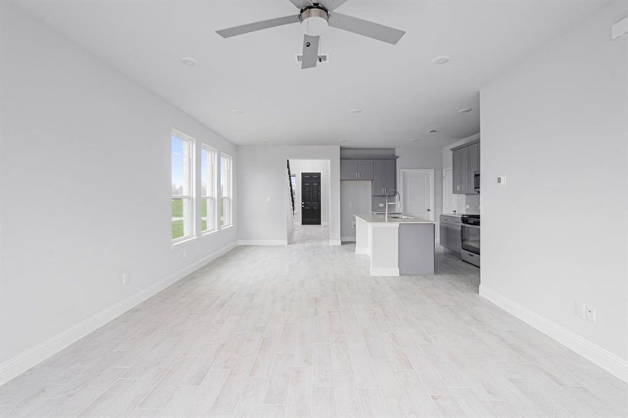 Unfurnished living room with light wood finished floors, visible vents, a sink, ceiling fan, and baseboards