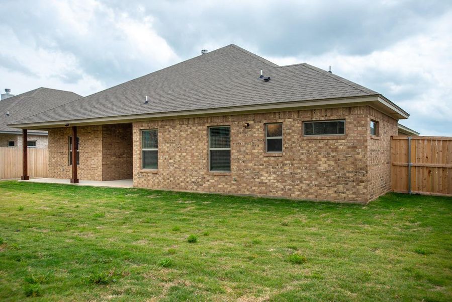 Rear view of property featuring roof with shingles, a lawn, a patio area, brick siding, and fence