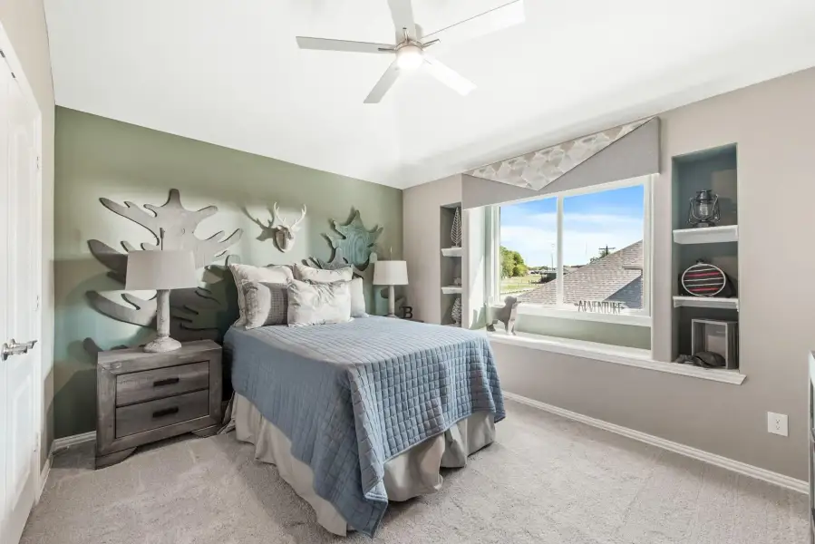 Bedroom with vaulted ceiling, ceiling fan, built-in shelves, and nature-themed wall decor above a blue bedspread