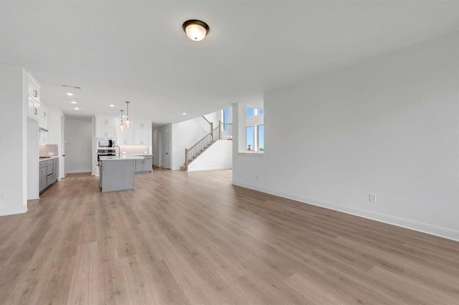 Open-concept living space with wide plank wood-finish flooring, recessed lighting, a modern kitchen with a center island, and a staircase featuring wood newel posts and spindles
