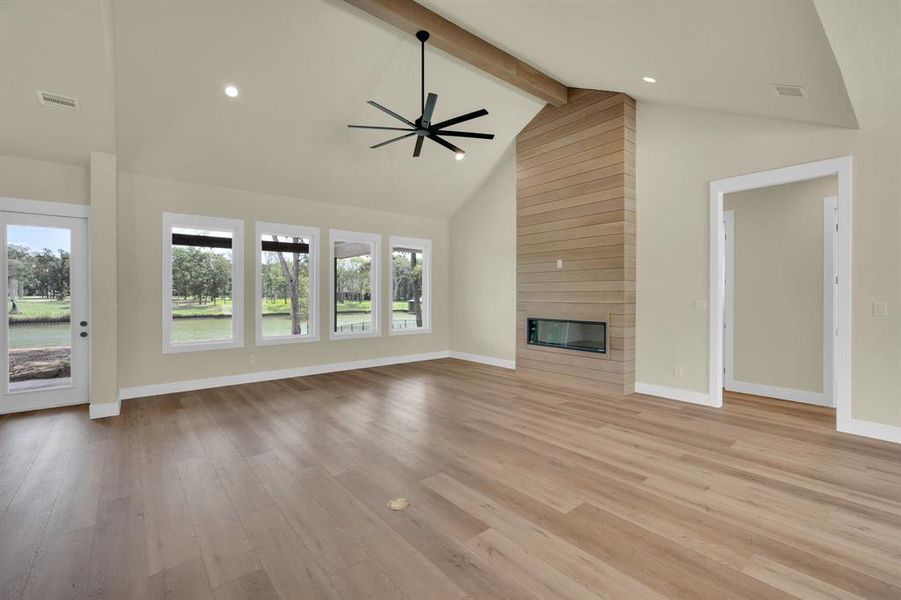 Unfurnished living room with beamed ceiling, light hardwood / wood-style flooring, high vaulted ceiling, and a large fireplace