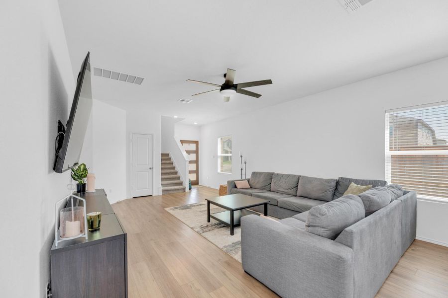 Living room featuring stairs, light wood finished floors, visible vents, and a ceiling fan