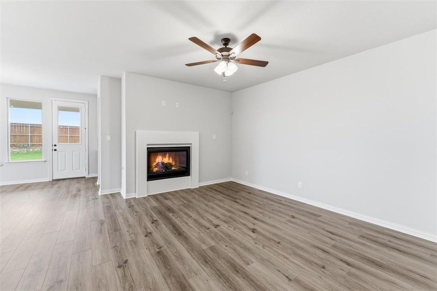 Living area featuring a modern fireplace with a white surround, wood-finish flooring, a ceiling fan with light fixture, and a glass-paneled exterior door