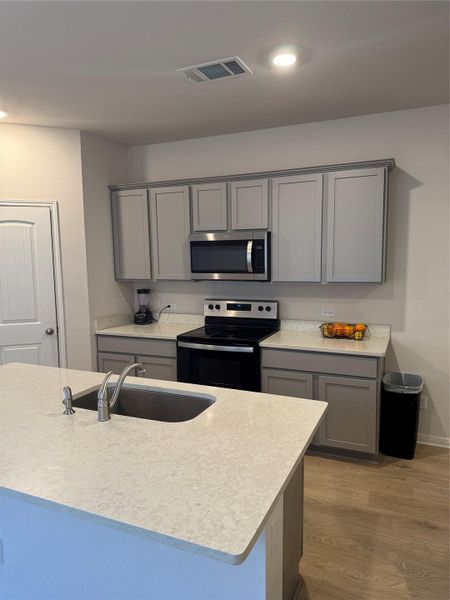 Kitchen with gray cabinets, stainless steel appliances, dark wood-type flooring, recessed lighting, and light stone countertops
