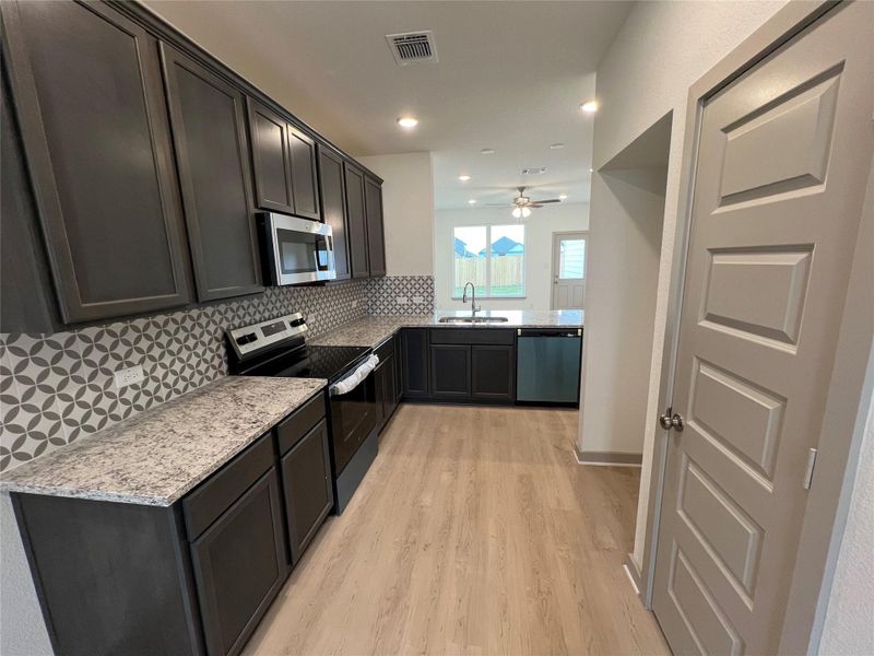 Kitchen featuring appliances with stainless steel finishes, light stone counters, tasteful backsplash, light wood-style floors, and recessed lighting Kitchen featuring appliances with stainless steel finishes, light stone counters, tasteful backsplash, light wood-style floors, and recessed lighting