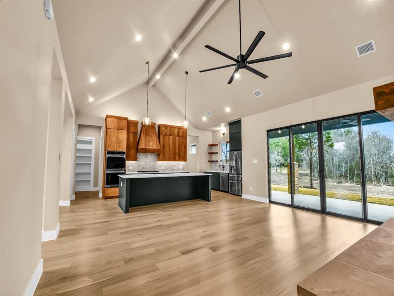 Kitchen with appliances with stainless steel finishes, ceiling fan, decorative light fixtures, high vaulted ceiling, and a large island