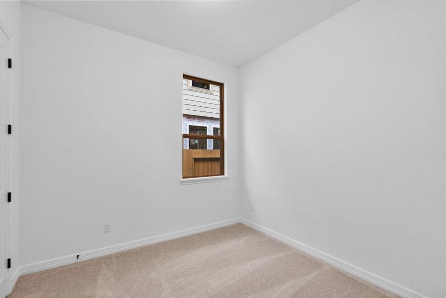 A comfortable third bedroom with plush carpet, a sun-filled window, and ample closet space.