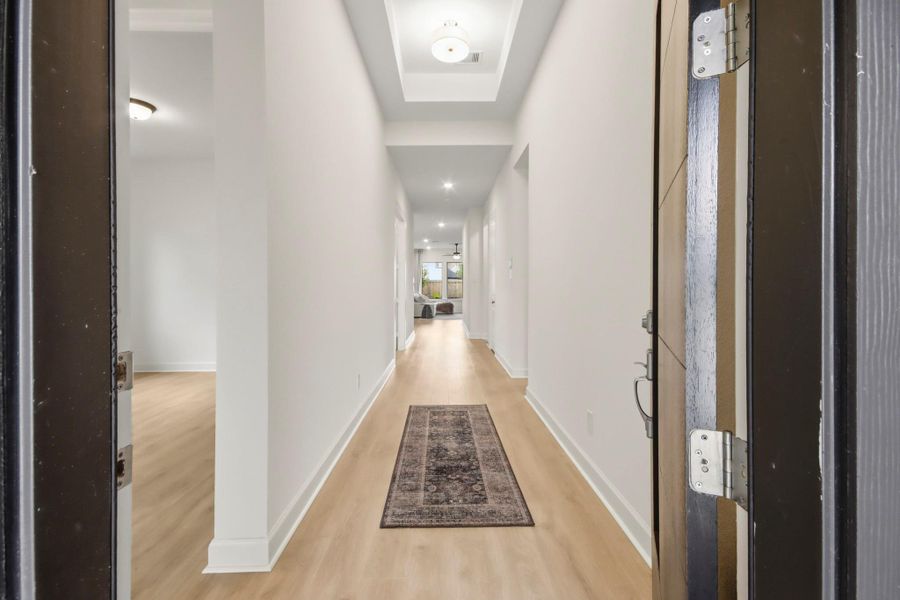 Inviting entryway features a long, well-lit hallway with elegant wood flooring and a stylish ceiling detail, leading to the main living area.
