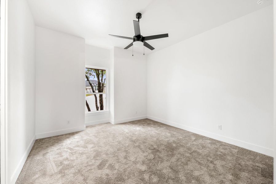 A well-lit bedroom features plush carpet and a modern ceiling fan, offering a comfortable personal retreat.