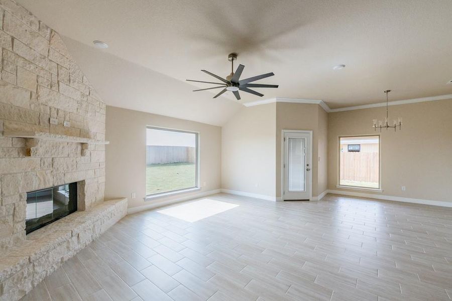 Unfurnished living room with wood finish floors, a fireplace, vaulted ceiling, ceiling fan, and a chandelier Unfurnished living room with wood finish floors, a fireplace, vaulted ceiling, ceiling fan, and a chandelier