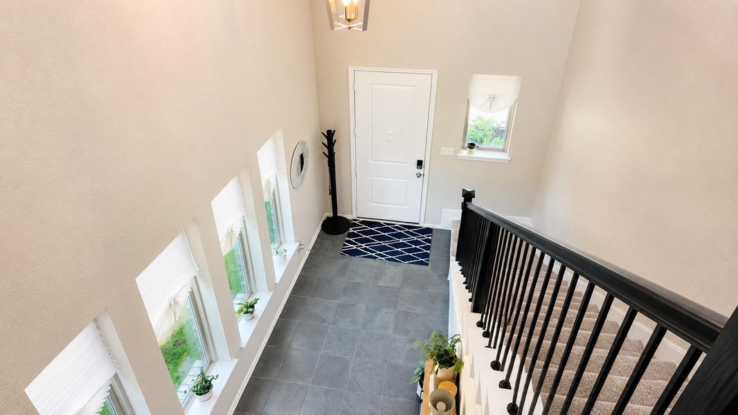 This two-story entryway features dark gray tile flooring and a carpeted staircase with black railings and balusters.