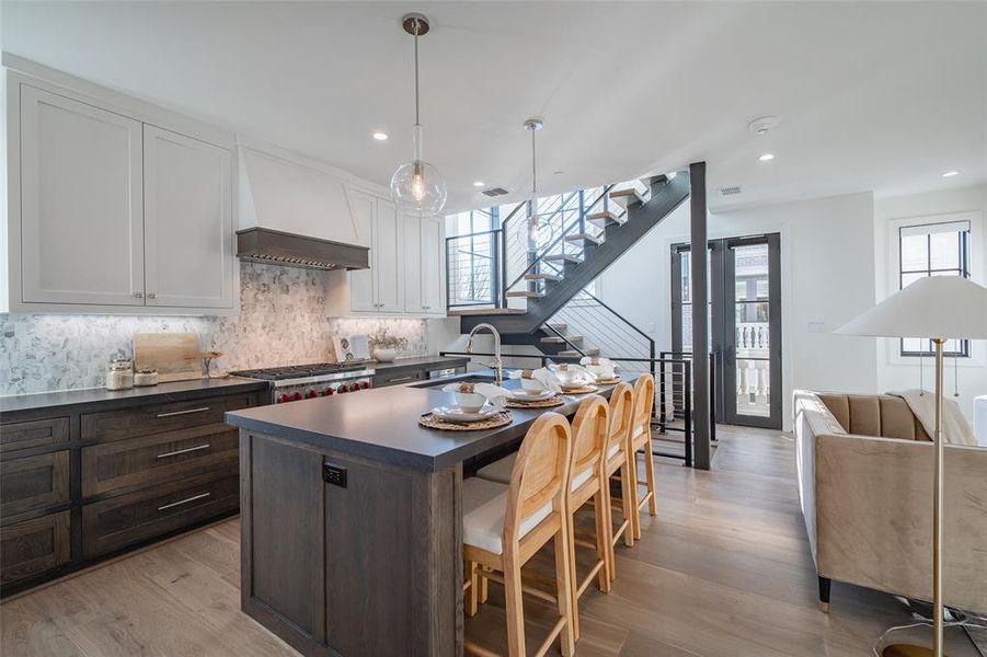 Kitchen featuring dark brown cabinetry, white cabinetry, pendant lighting, a kitchen bar, and custom exhaust hood