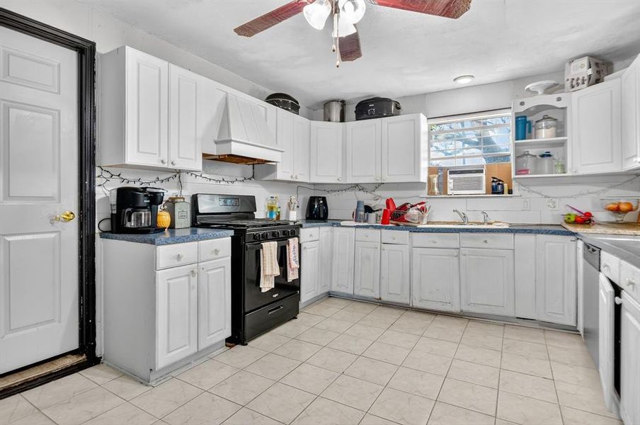 Kitchen featuring black gas stove, white cabinetry, decorative backsplash, custom range hood, and dark countertops Kitchen featuring black gas stove, white cabinetry, decorative backsplash, custom range hood, and dark countertops