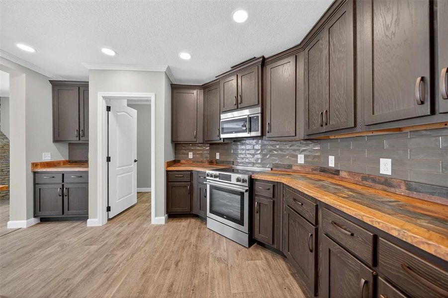 Kitchen with appliances with stainless steel finishes, crown molding, wooden counters, tasteful backsplash, and a textured ceiling Kitchen with appliances with stainless steel finishes, crown molding, wooden counters, tasteful backsplash, and a textured ceiling