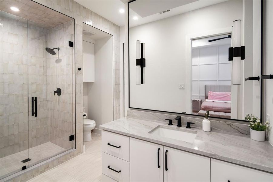 Beautifully appointed second-floor ensuite bathroom featuring an expansive vanity, designer lighting, and sleek modern hardware. A striking wall of luxury tile with bold black accents highlights the walk-in shower, while additional built-in storage enhances functionality. This suite also includes an oversized walk-in closet, offering exceptional storage and organization.
