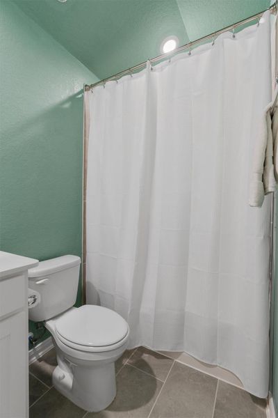 Bathroom featuring a white toilet, white vanity with cabinet storage, a shower with a white curtain, recessed lighting, and large format tile flooring Bathroom featuring a white toilet, white vanity with cabinet storage, a shower with a white curtain, recessed lighting, and large format tile flooring