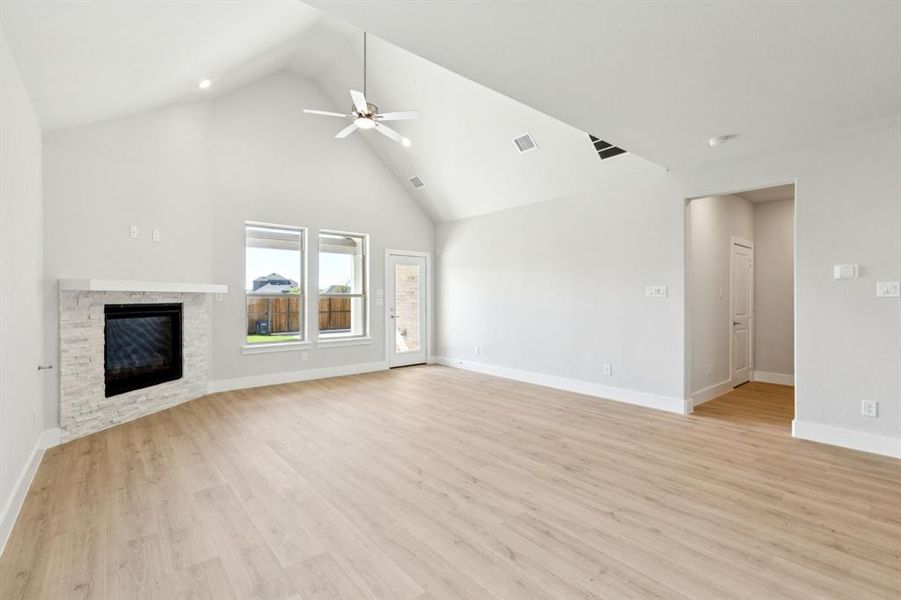 Unfurnished living room featuring high vaulted ceiling, light wood-style floors, a fireplace, and a ceiling fan Unfurnished living room featuring high vaulted ceiling, light wood-style floors, a fireplace, and a ceiling fan