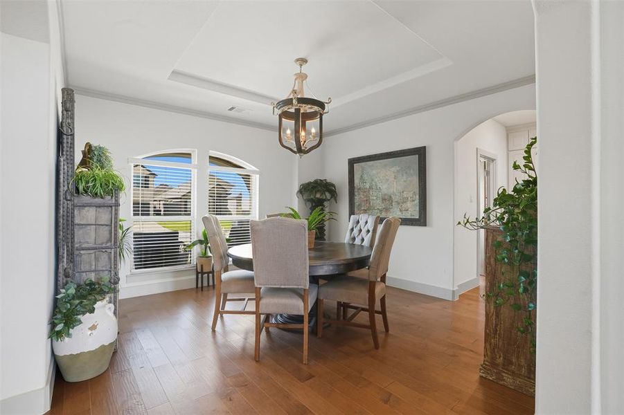 Dining space with a raised ceiling, hardwood / wood-style flooring, a chandelier, arched walkways, and crown molding Dining space with a raised ceiling, hardwood / wood-style flooring, a chandelier, arched walkways, and crown molding
