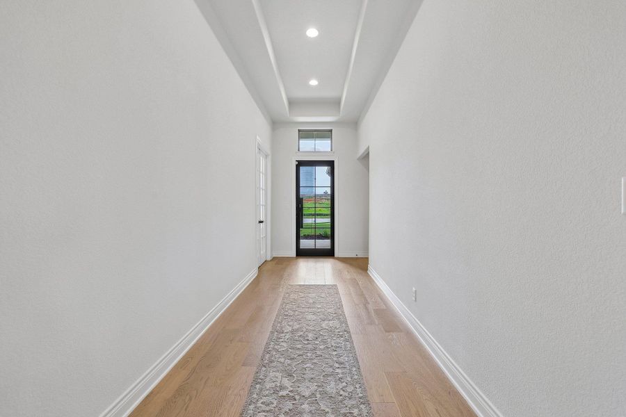 Foyer entry featuring a black multi-pane glass door with transom window, light wood-finish flooring, and a coffered ceiling with recessed lighting